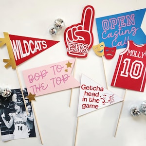 Könnte beinhalten: Eine Sammlung von Partydekorationen, darunter Wimpel, ein Schaumstoff-Finger und ein Trikot. Die Wimpel zeigen Texte wie "Wildcats" und "Bop to the Top". Ein Foto einer Person mit einem Trikot ist ebenfalls enthalten. Diskokugeln sind um die Dekorationen verstreut.