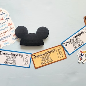 Puede incluir: Una colección de artículos temáticos de Disneyland, que incluyen boletos de Monorrail, pegatinas con atracciones del parque y una silueta negra de Mickey Mouse. Los boletos son de color beige y azul, con el texto "Disneyland Monorail".
