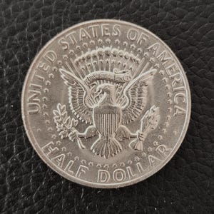 Może przedstawiać: Srebrna moneta półdolarowa z napisami "United States of America" i "Half Dollar" otaczającymi emblemat orła. Moneta jest w dobrym stanie, z wyraźnymi szczegółami projektu.