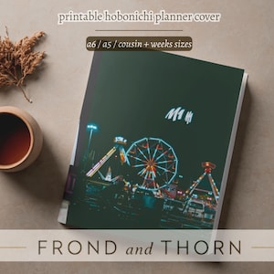 Op de afbeelding: Een donkergroene planner cover met een nachtelijke kermis scène met een reuzenrad en andere attracties. De tekst "printable hobonichi planner cover" en "FROND and THORN" worden weergegeven. Verkrijgbaar in a6, a5, cousin en weekmaten.