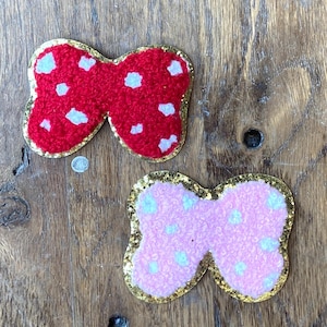 Puede incluir: Dos formas de mariposa de fieltro con ribete de purpurina dorada. Las mariposas son rojas y rosas con lunares blancos.