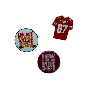 Puede incluir: Tres pines redondos con dise&ntilde;os rojos, blancos y dorados. El primer pin dice "In My Travis Kelce Era". El segundo pin dice "Karma Is The Guy On The Chiefs". El tercer pin es una camiseta de f&uacute;tbol roja con el n&uacute;mero 87 y el nombre "Swift" en la espalda.