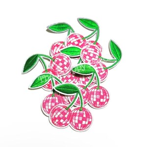 May include: A group of pink and white cherry-shaped iron-on patches with a disco ball design. The cherries have green stems and leaves.