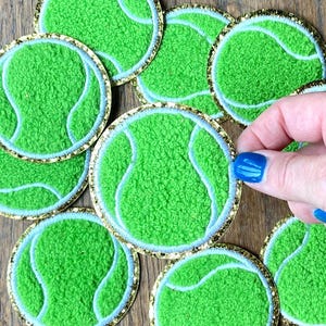 Könnte beinhalten: Ein Set mit neun grünen und weißen Tennisball-Patches mit goldfarbenem Glitzerbesatz. Die Patches sind aus einem flauschigen Material gefertigt und eignen sich perfekt, um jedem Projekt eine sportliche Note zu verleihen.