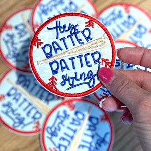May include: Close-up of a red, white, and blue embroidered patch with a baseball bat and the text "Hey Batter Batter Swing".