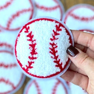 Può includere: Un set di toppe da baseball in feltro bianco e rosso. Le toppe sono rotonde e hanno uno sfondo bianco con cuciture rosse.