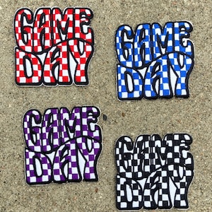 May include: Four iron-on patches with the text "GAME DAY" in a checkered pattern. The patches are red and white, blue and white, purple and white, and black and white.