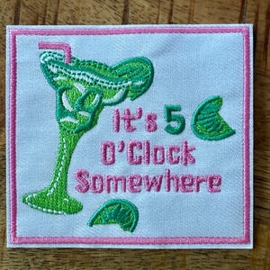 May include: Embroidered patch with a green margarita glass and a pink straw. The text "It's 5 O'Clock Somewhere" is in pink. The patch has a white background with a pink border, and two lime wedges.
