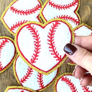 May include: A set of heart-shaped patches with a baseball design. The patches are white with red stitching and a gold glitter border.