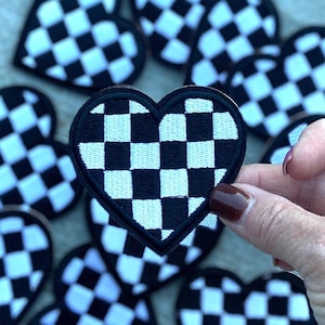 Op de afbeelding: Een set zwarte en witte geruite hartvormige patches. De patches zijn gemaakt van stof en hebben een gestikte rand.