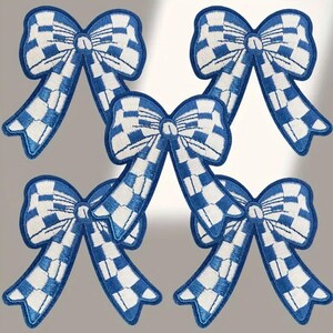 May include: Five blue and white checkered bow patches. The bows are embroidered with white thread on a blue fabric.