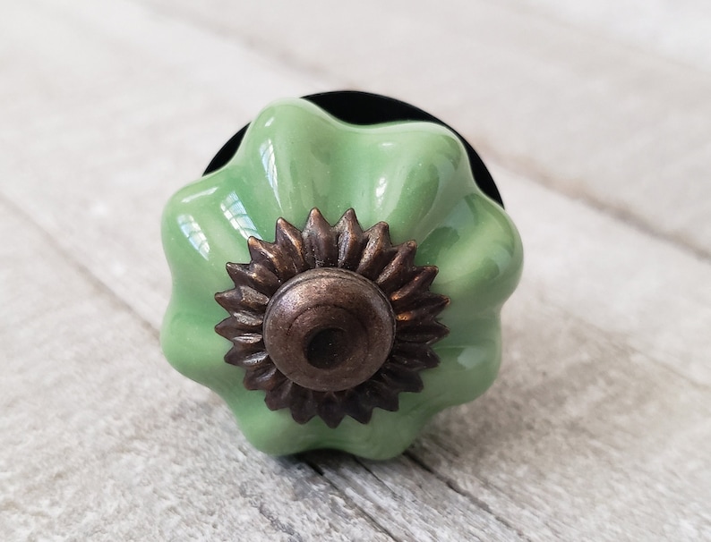 May include: A green ceramic cabinet knob with a decorative bronze flower design.