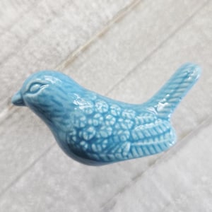 May include: A light blue ceramic bird figurine. The bird has detailed feather patterns and a textured surface. The figurine is a decorative item, likely for home decor or a collection.
