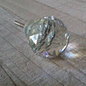 May include: A clear crystal cabinet knob with a faceted design. The knob has a silver metal screw.
