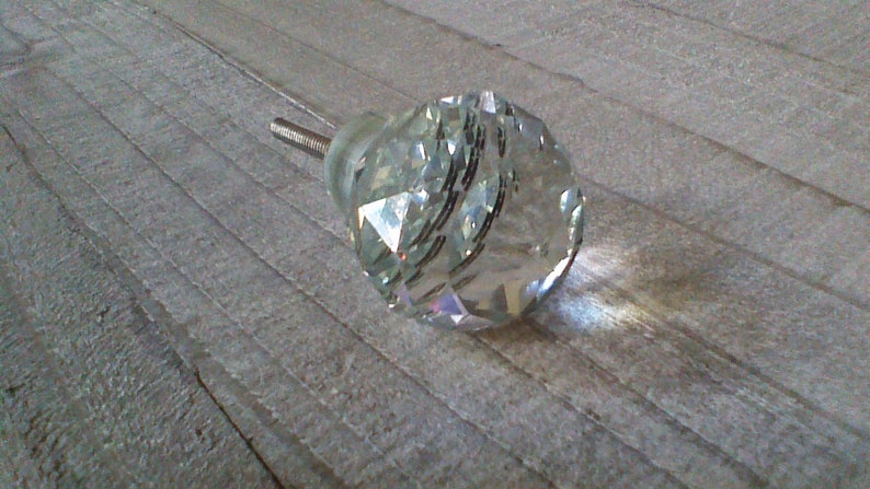 May include: A clear crystal cabinet knob with a faceted design. The knob has a silver metal screw.