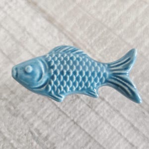 Peut inclure: Une figurine de poisson en céramique bleu clair avec des motifs détaillés d'écailles et d'ailerons. Le poisson décoratif est de couleur unie et a une finition brillante. Le poisson mesure environ 10 cm de long.