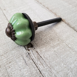 May include: A green ceramic cabinet knob with a metal base and a black screw. The knob has a rounded, pumpkin-like shape.