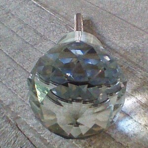 May include: A clear glass crystal knob with a faceted design. The knob has a silver metal stem.