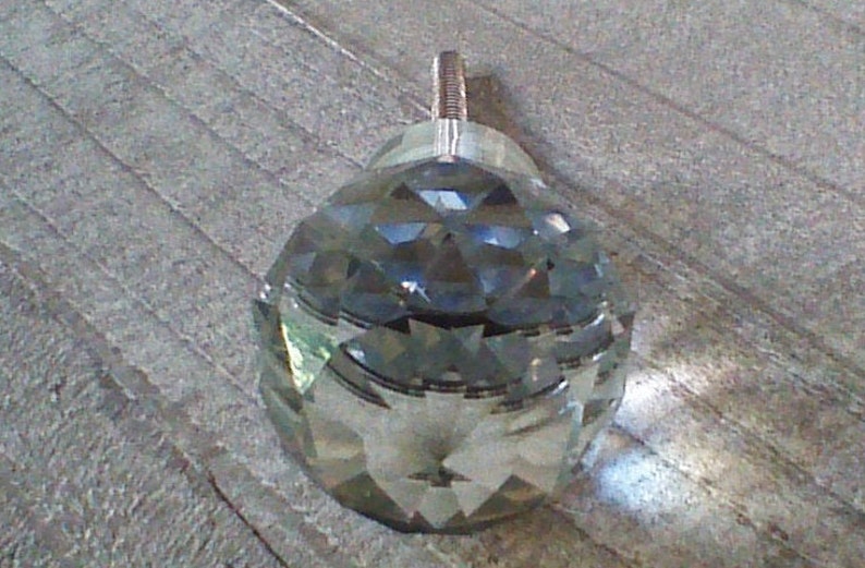 May include: A clear glass crystal knob with a faceted design. The knob has a silver metal stem.