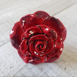 May include: A red ceramic rose with a glossy finish. The rose is a single bloom with multiple layers of petals.