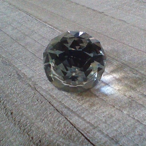 May include: A clear glass crystal ball with many facets, reflecting light on a wooden surface.