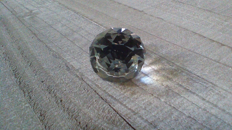 May include: A clear glass crystal ball with many facets, reflecting light on a wooden surface.