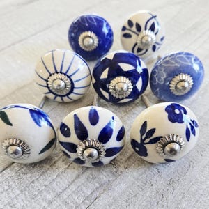 Puede incluir: Un conjunto de ocho pomos de cerámica para armarios. Los pomos son blancos con diseños florales azules y herrajes metálicos plateados. Los diseños incluyen variaciones en azul liso, floral y estampado. Ideales para muebles.