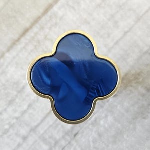 May include: A clover-shaped cabinet knob with a gold-colored trim and a deep blue center. The blue center has a marbled appearance. The knob is designed for furniture and home decor.