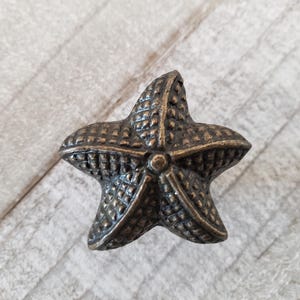 May include: A bronze-colored starfish-shaped cabinet knob with a detailed textured surface.