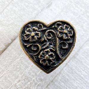 May include: A heart-shaped brass cabinet knob with a black floral design. The knob has a raised, textured design of three flowers and leaves.