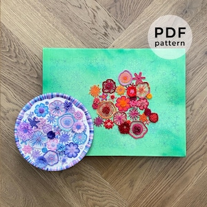 Peut inclure: Une toile verte avec un motif en forme de cœur de fleurs brodées dans des tons de rouge, orange et rose. Une assiette séparée avec des fleurs brodées dans des tons de violet, bleu et rose est également visible. Le texte "PDF pattern" est visible dans le coin supérieur droit de l'image.