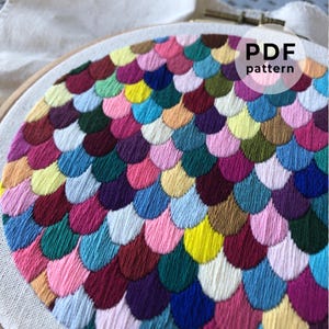 May include: A colourful embroidery pattern of overlapping, half-circle shapes in a variety of colours, including pink, blue, green, yellow, and purple. The pattern is stitched on a white fabric and is framed in a wooden embroidery hoop. The text "PDF pattern" is visible in the top right corner of the image.