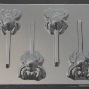 May include: A clear plastic mold for making four spider-shaped lollipops. The mold has four cavities, each with a spider design and a stick holder.