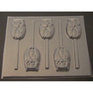 May include: A clear plastic mold for making six owl-shaped lollipops. The mold has six cavities, each with an owl design and a stick holder.