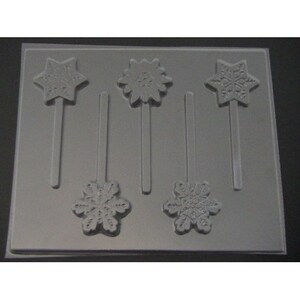 May include: A gray plastic mold for making snowflake lollipops. The mold has five cavities, each with a snowflake design and a stick.