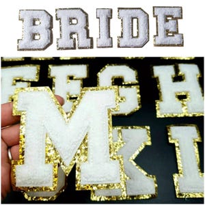 May include: White felt letters with gold glitter trim. The letters spell out "BRIDE".