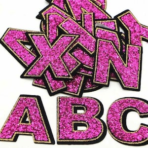 May include: Pink glitter letters of the alphabet A, B, and C with black outlines. The letters are individually cut out and have a sparkly finish.