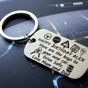 May include: A silver keyring with a rectangular tag engraved with the text "HAPPY BIRTHDAY ALEX" and driving-related icons. The keyring includes a key ring and is designed as a gift.