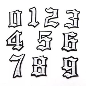 May include: Set of ten white iron-on patches with black outlines of the numbers 0 through 9 in a gothic font style.