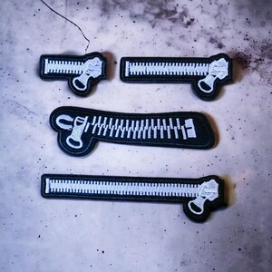 Peut inclure: Quatre patchs de fermeture éclair brodés en noir et blanc. Les patchs sont de tailles et d'orientations différentes. Les dents de la fermeture éclair sont blanches et le reste du patch est noir.