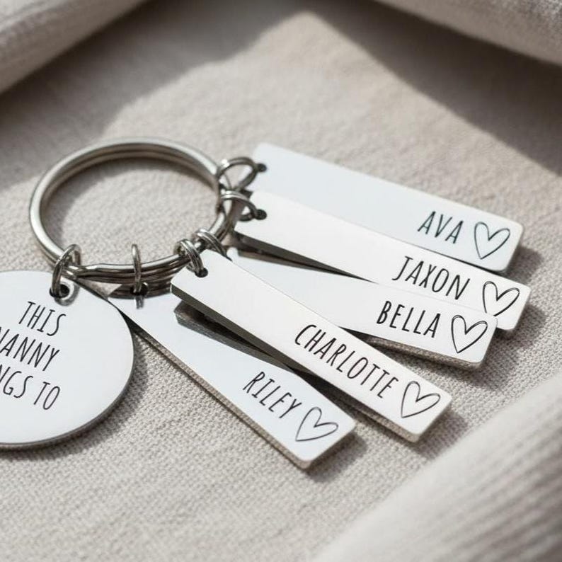 Puede incluir: Un llavero plateado con m&uacute;ltiples etiquetas rectangulares y una etiqueta redonda. Las etiquetas rectangulares est&aacute;n grabadas con nombres y un s&iacute;mbolo de coraz&oacute;n. La etiqueta redonda dice "THIS NANNY BELONGS TO".