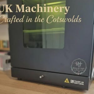 Puede incluir: M&aacute;quina negra con ventana de cristal, con el texto "UK Machinery Crafted in the Cotswolds". La m&aacute;quina tiene un logotipo "Riley & Jojo" y una etiqueta "Made in Britain". Tambi&eacute;n es visible un s&iacute;mbolo de advertencia.