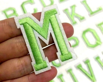 May include: Green felt letter M with a white outline. The letter is part of a set of green felt letters with white outlines.