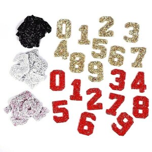 May include: Assortment of iron-on numbers in red, gold, and silver glitter. The numbers range from 0 to 9.