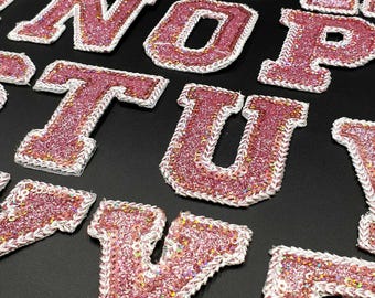 Könnte beinhalten: Rosa glitzernde Buchstaben des Alphabets, von A bis Z, mit einem weißen Umriss. Die Buchstaben sind mit Pailletten bestickt und perfekt für Bastelprojekte.