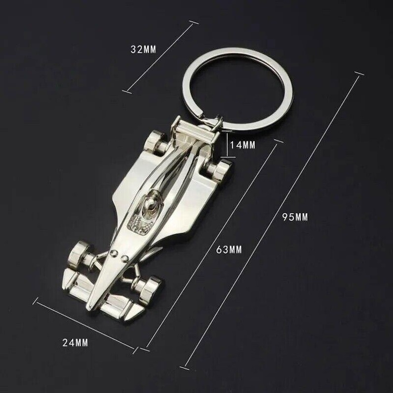 May include: A silver-colored keychain shaped like a race car. The keychain measures 9.5 cm long, 6.3 cm wide, and 3.2 cm tall. The keychain has a ring for attaching keys.