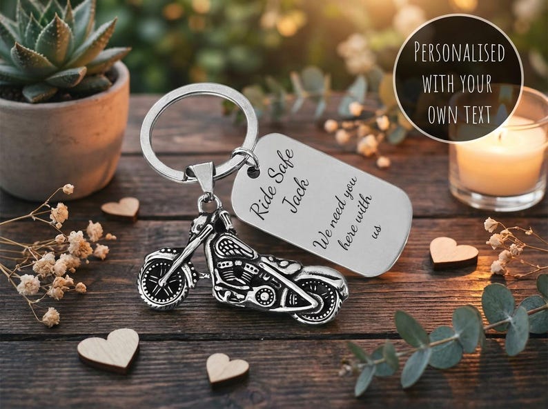 May include: Silver motorcycle keychain with a rectangular tag. The tag is engraved with the words "Ride Safe Jack" and "We need you here with us". The keychain is on a wooden surface with decorative hearts and a succulent plant.