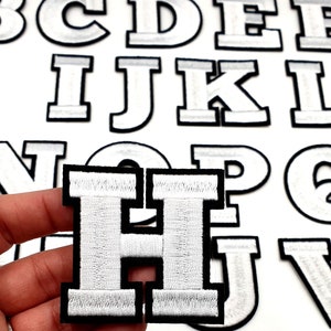 May include: White felt letter patches with black outlines. The letters are H and I.