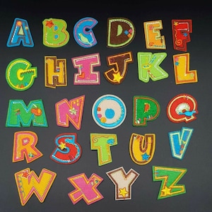 May include: A set of 26 colorful felt alphabet letters with embroidered details. Each letter is individually cut out and features a different design, such as a bird, a star, or a flower.