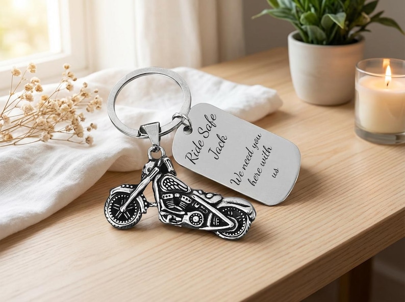 May include: A silver motorcycle keychain with a detailed bike charm and a rectangular tag. The tag is engraved with the words "Ride Safe Jack, We need you here with us". The keychain is on a wooden surface.